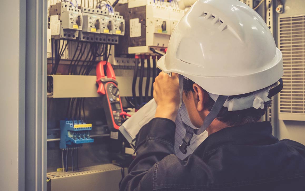 Funcionário usando capacete de segurança examinando controles eletrônicos