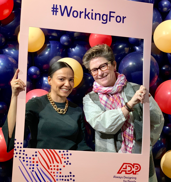 Two employees pose in large photo frame during a celebration