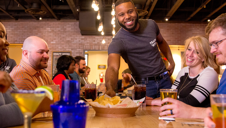 Chili’s Server serving nachos to table of happy Guests