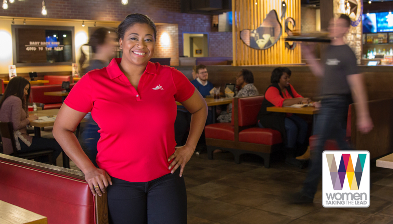 Female Chili’s Team Member proudly standing in a Chili’s restaurant