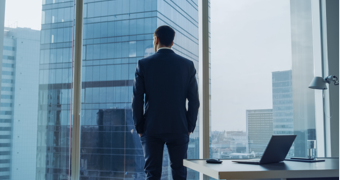 A man looks out the window of a high-rise office building