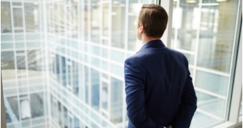 A man looks out the window of a high-rise office building