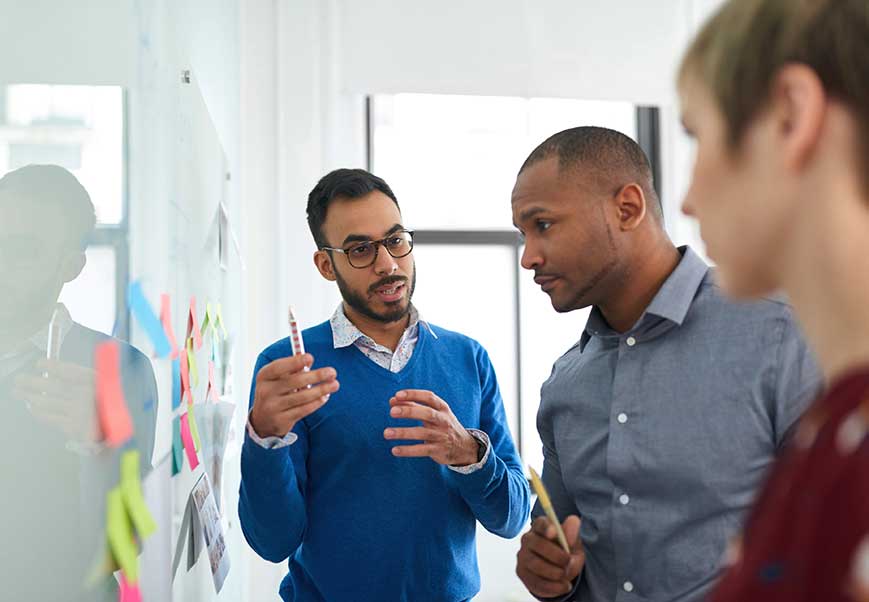 Three people discussing post it notes on a white board