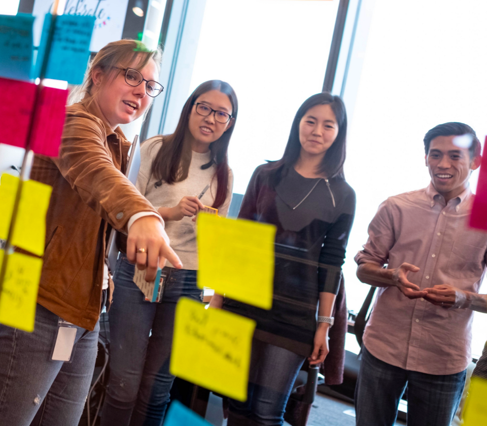 ApprenticeshipDevelopment_blogscreenshot@2x A Pinterest employees, in a group of employees, pointing at sticky notes on a wall