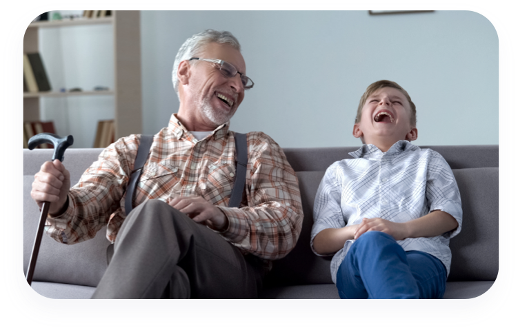 Grandfather and grandson sitting on couch laughing.