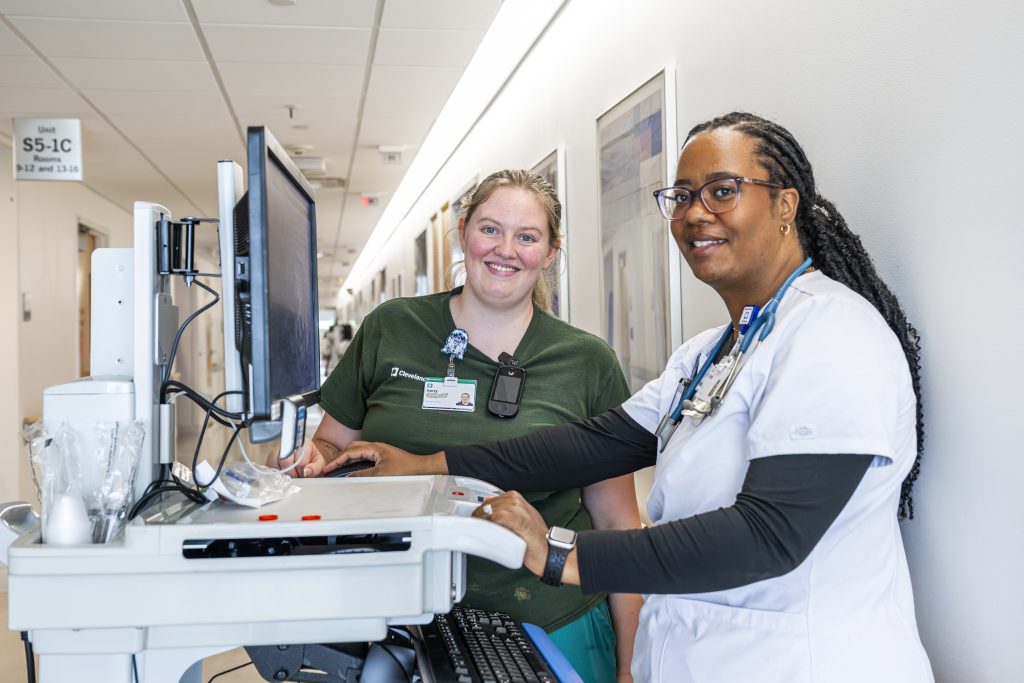 Two Cleveland Clinic healthcare staff smiling while using a computer on a mobile workstation.