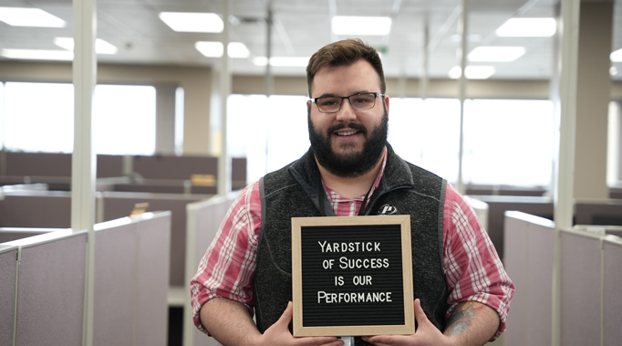 Man holding sign saying Yardstick of Success is our Performance