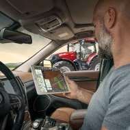 Un hombre sentado en la cabina de su tractor mirando información en la pantalla de un tablet.