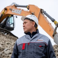 Un hombre con casco protector en una obra de construcción con una excavadora mecánica de fondo.