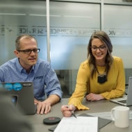 Un colaborador y una colaboradora administrativos sentados frente a un escritorio trabajando juntos.