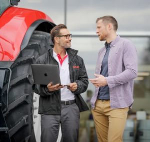A CNH salesperson talks with customers as they stand beside a large agricultural machine.