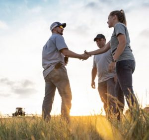 A CNH Service and Support employee shakes hands with farmers in a field.