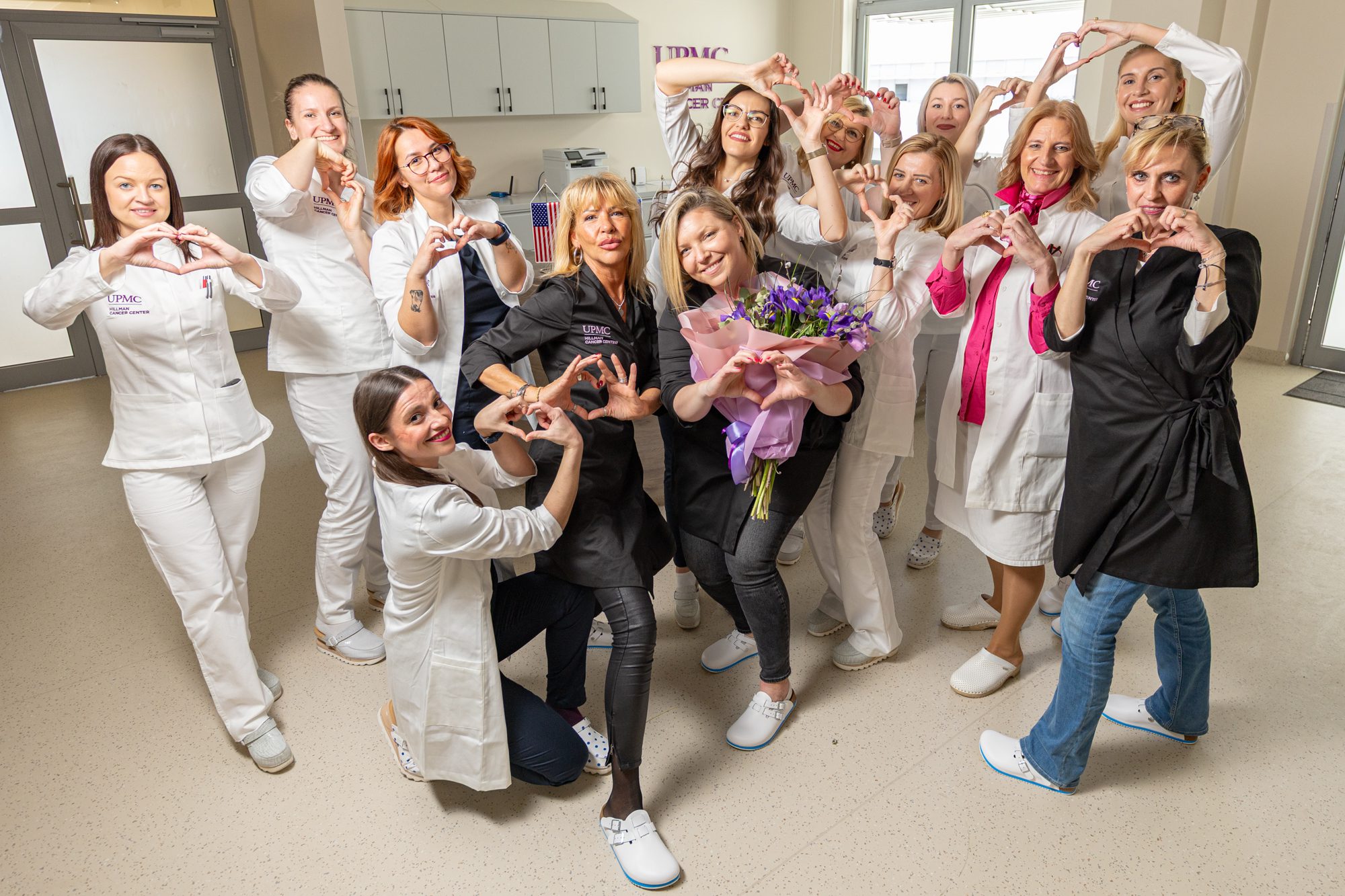 Group of women in a hospital room holding up heart hands sign.