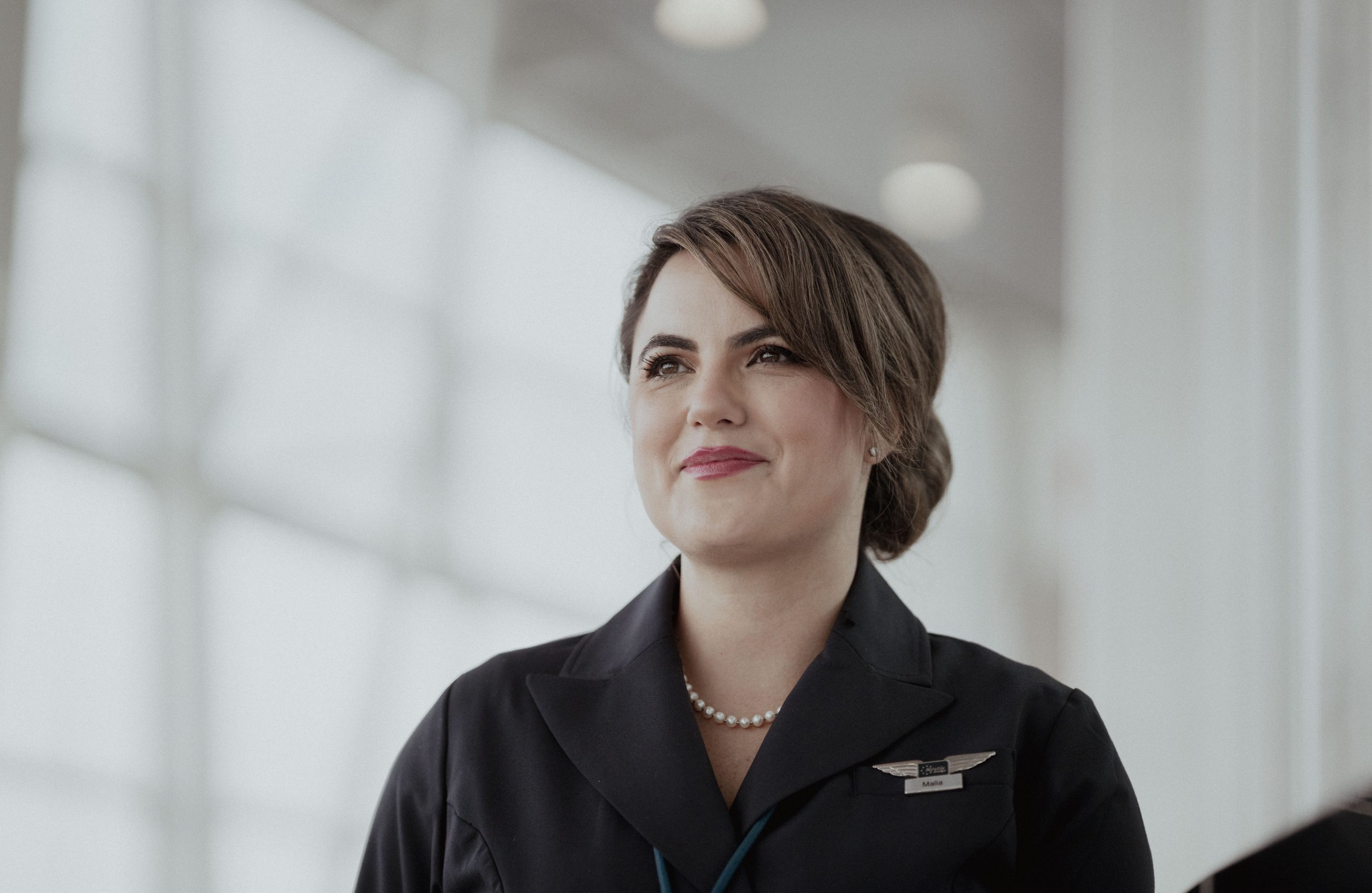 A flight attendant with a cheerful smile standing in front of a jet.