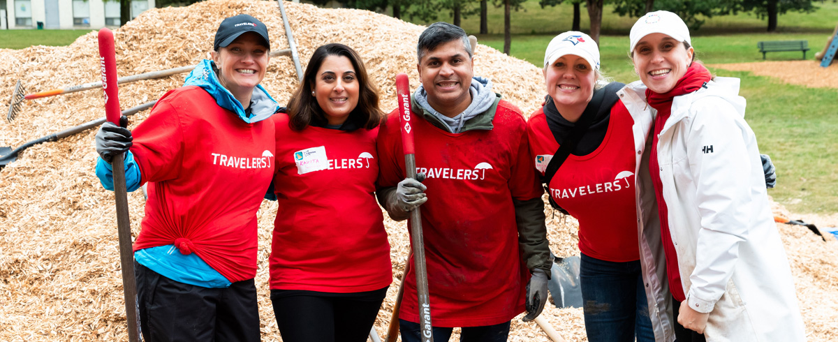 A diverse group of professionals engaged in volunteer work outside, reflecting a collaborative culture and a workplace environment where community service is important.