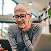 Mature woman in her home with a laptop in front of her and looking at her phone.