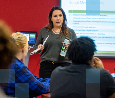 A female high school teacher instructing a diverse group of high school students in a classroom setting