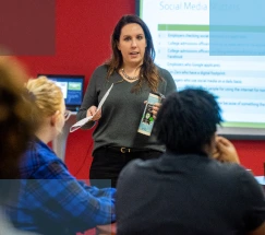 A female high school teacher instructing a diverse group of high school students in a classroom setting