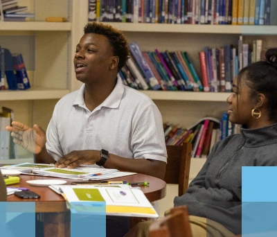 A male African American high school student and a female African American high school student sitting at a table in a library