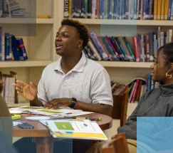 A male African American high school student and a female African American high school student sitting at a table in a library