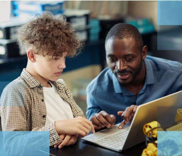 Male high school teacher helping a male high school student working on a laptop computer