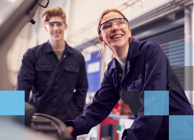 A smiling male and a smiling female high school student working under the hood of an automobile in an auto shop setting