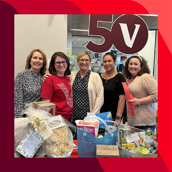 Jill and four other people stand behind a table with various gift baskets, with a large 