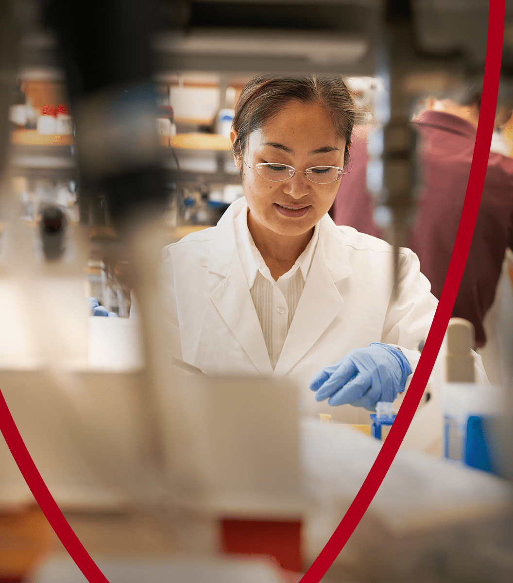 A scientist in a white lab coat and gloves conducts research in a laboratory, focusing on an experiment.