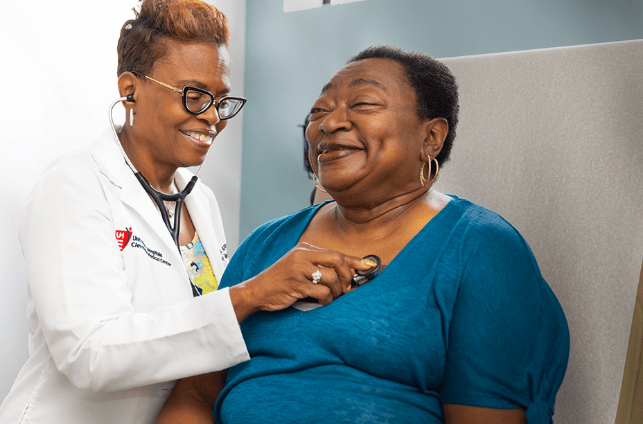 A smiling healthcare professional in a white coat uses a stethoscope to check a happy patient in a clinical setting.