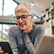 Mature woman in her home with a laptop in front of her and looking at her phone.
