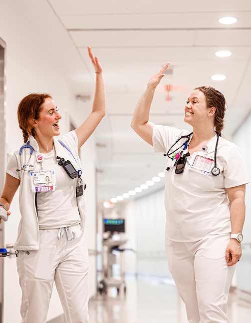 Two smiling female Cleveland Clinic caregivers high fiving in a hospital hallway