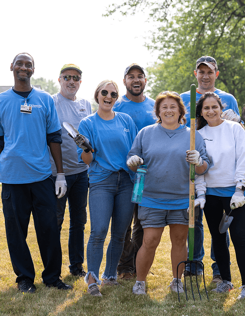 A group of Cleveland Clinic caregivers in jeans and t-shirts holding gardening tools and working in a park-like setting