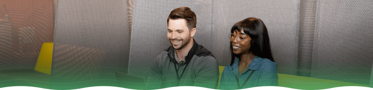 Two people sitting in modern office booth, looking at a laptop on a small table