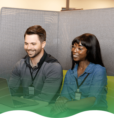 Two people sitting in modern office booth, looking at a laptop on a small table