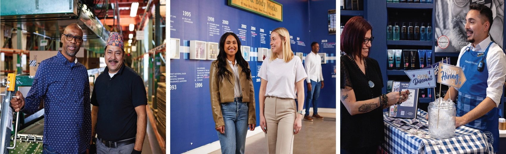 Two employees stand smiling in front of a conveyor belt inside a distribution center. Two associates walk smiling through a corporate office hallway displaying a timeline of Bath & Body Works history. A Bath & Body Works associate in a blue gingham apron chats and smiles with a candidate at a now hiring display in-store.