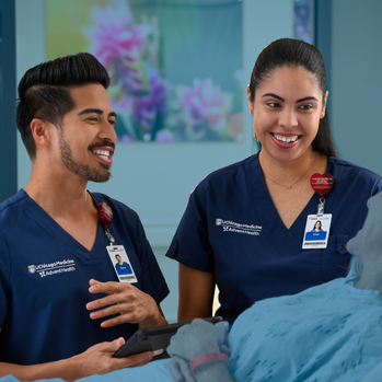 A smiling male and a smiling female nursing professional caring for a patient