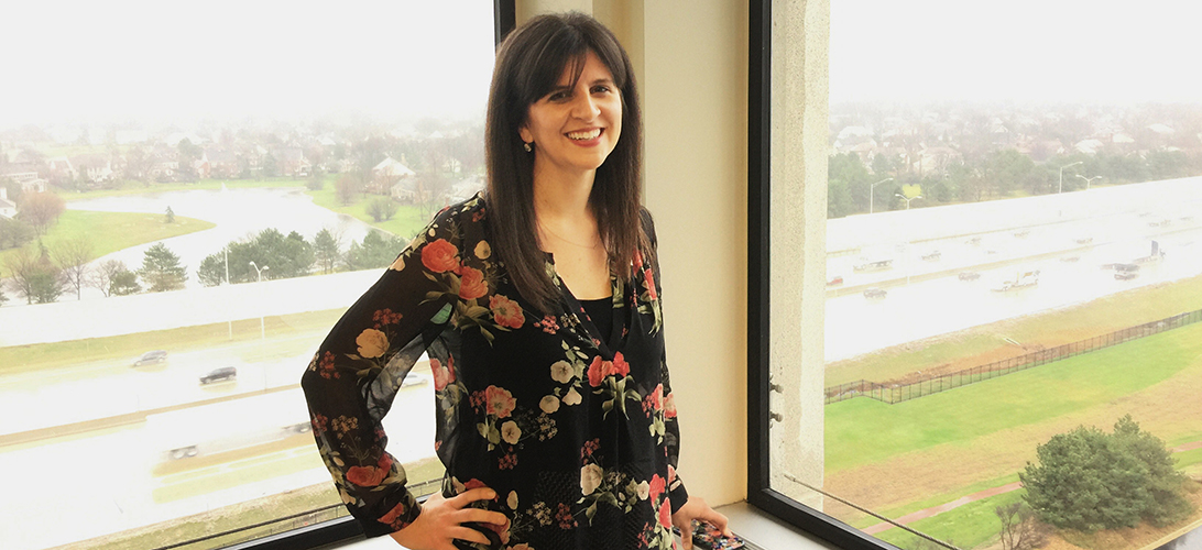 Standing female Allstater in front of windows, hand on hip, smiling at the camera.
