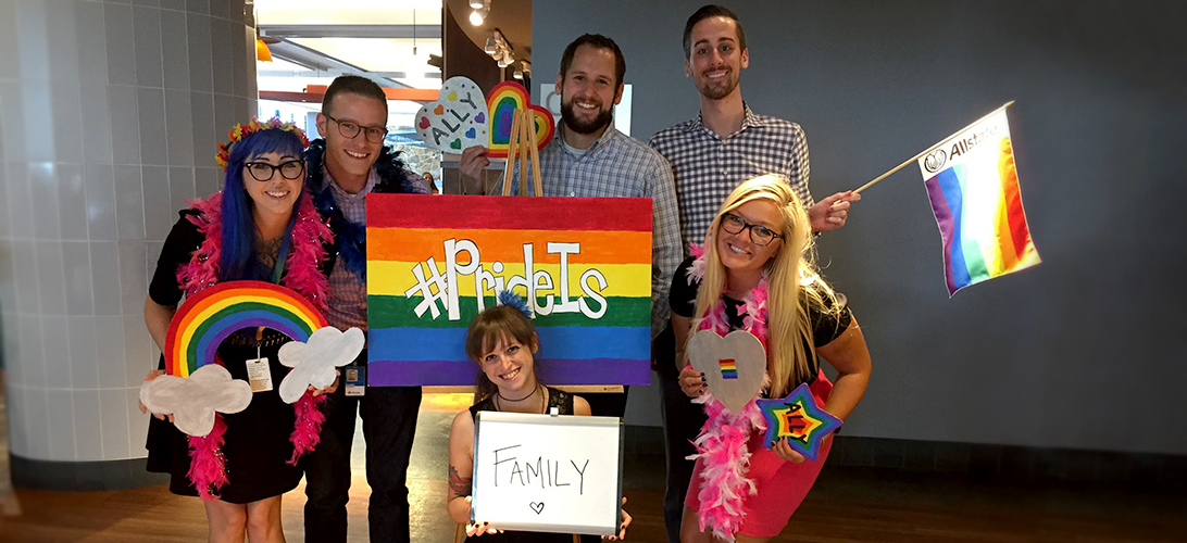 Group of diverse Allstaters holding rainbow flags and banners.