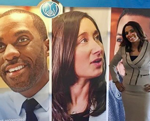 Smiling Allstate employee standing in front of pictures of diverse faces.