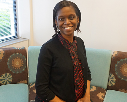 Female Allstate employee sitting on a couch, smiling at the camera.