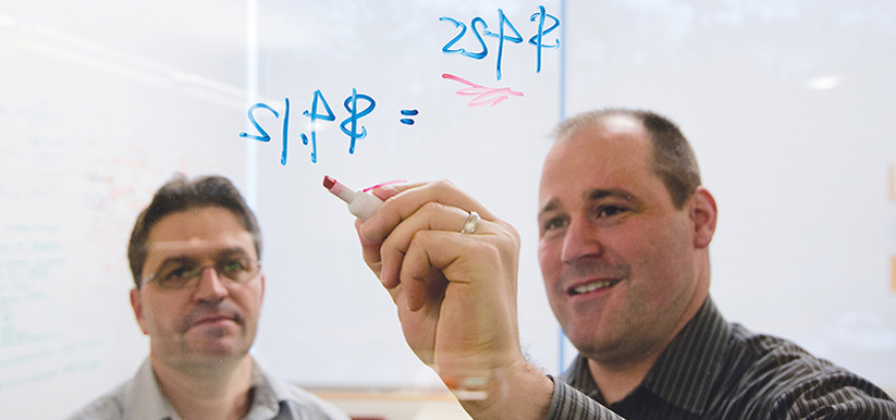 Two men making calculations on a glass window