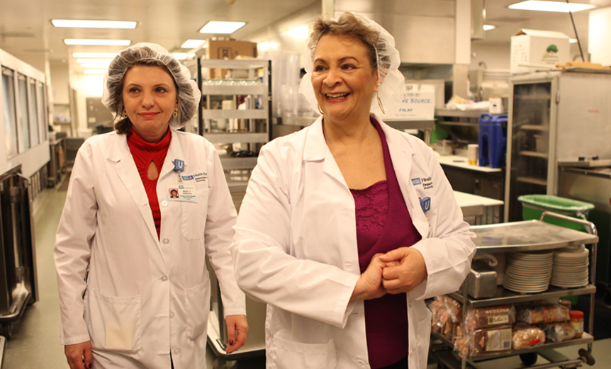 Smiling food service employees in cafeteria kitchen.