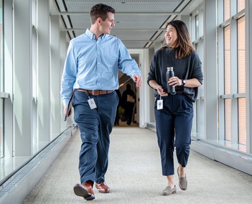 Two Vanguard crew members walking down a glass hallway in their office, laughing and talking