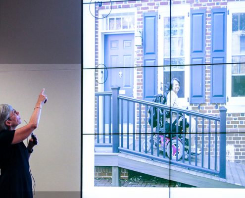 Picture of Susan Tachau at the event, showing a photo of a woman in a wheelchair who is outside her home that was equipped with accessibility features.