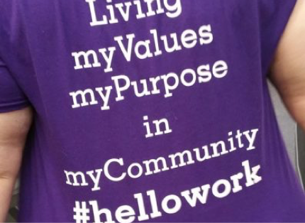 woman wearing purple T-shirt with the words "Living my Values, my Purpose in my Community. #hellowork