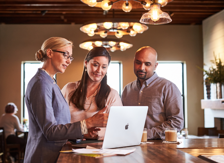 A financial advisor points to her laptop screen while speaking with a woman and man