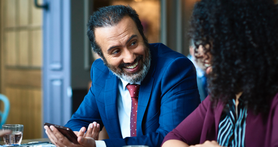 A man and woman at a table looking at a mobile phone.