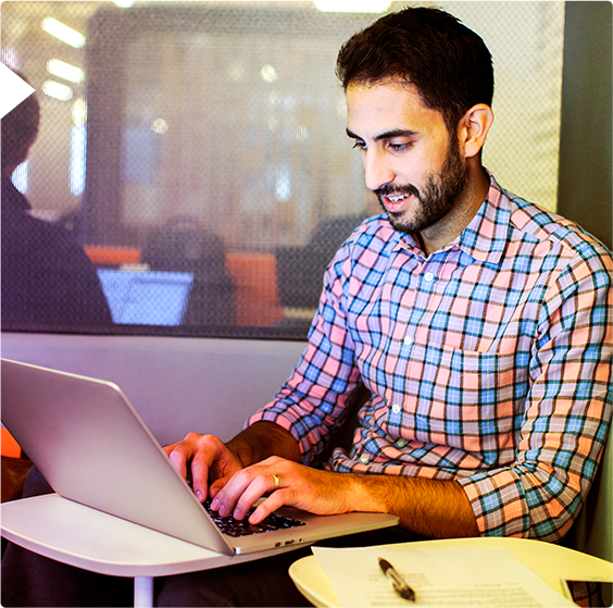 A male employee typing on his laptop while seated in an office.